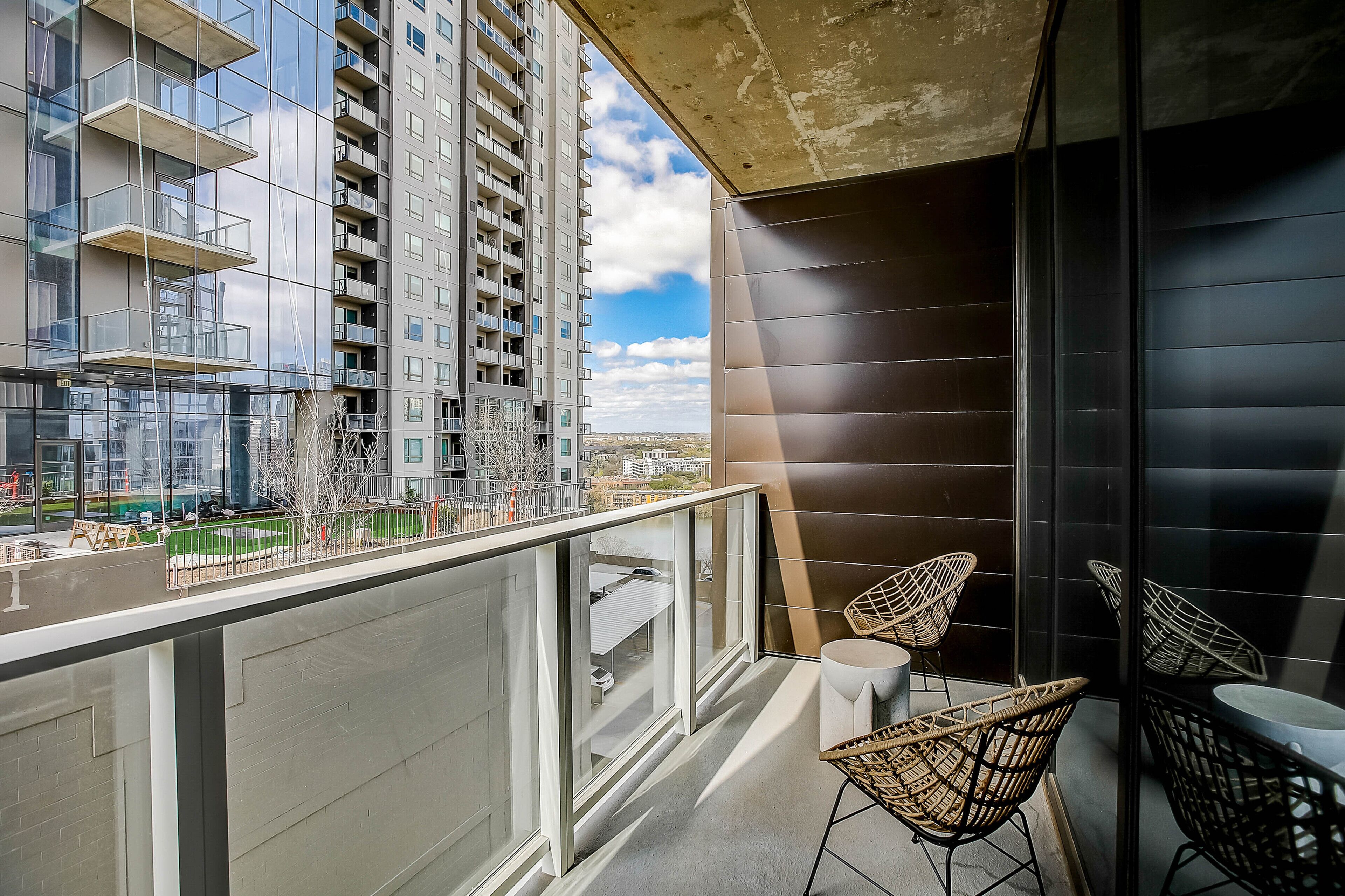 A balcony with glass railings, wicker chairs, and a view of high-rise buildings.