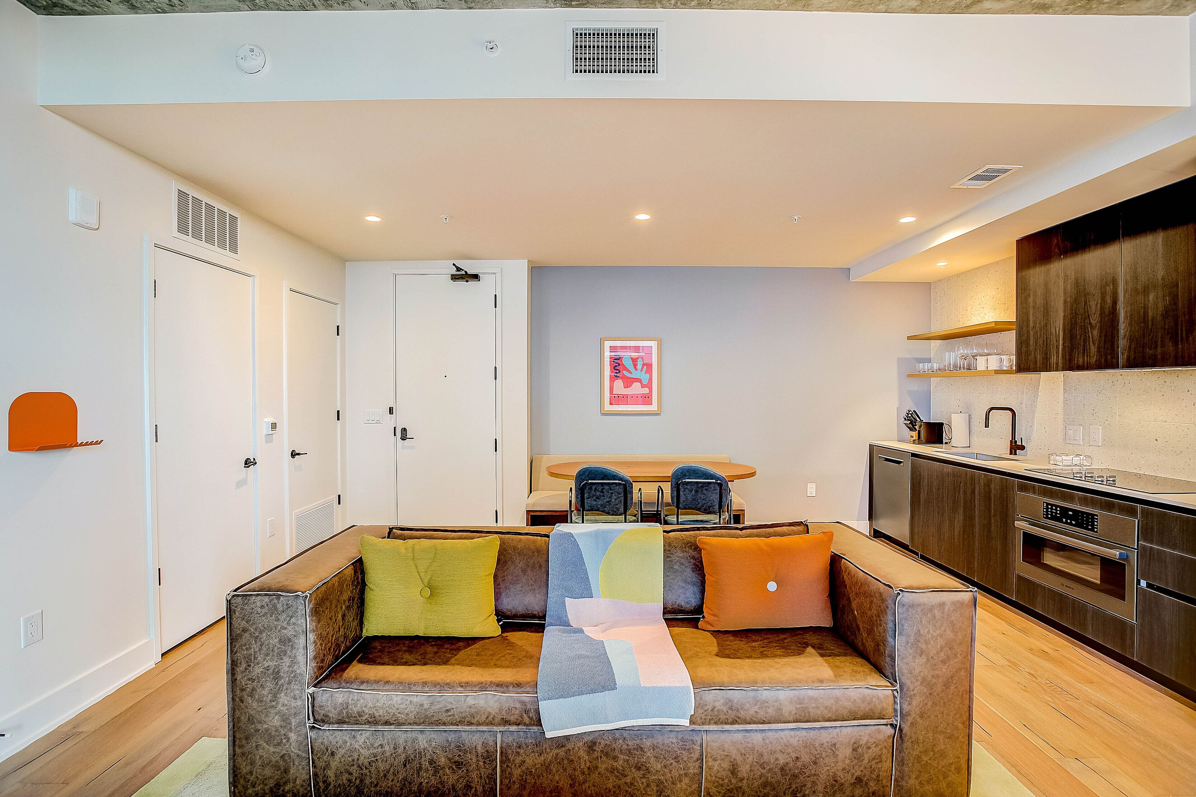 A modern living room with a sofa, a dining table, and a kitchen area.