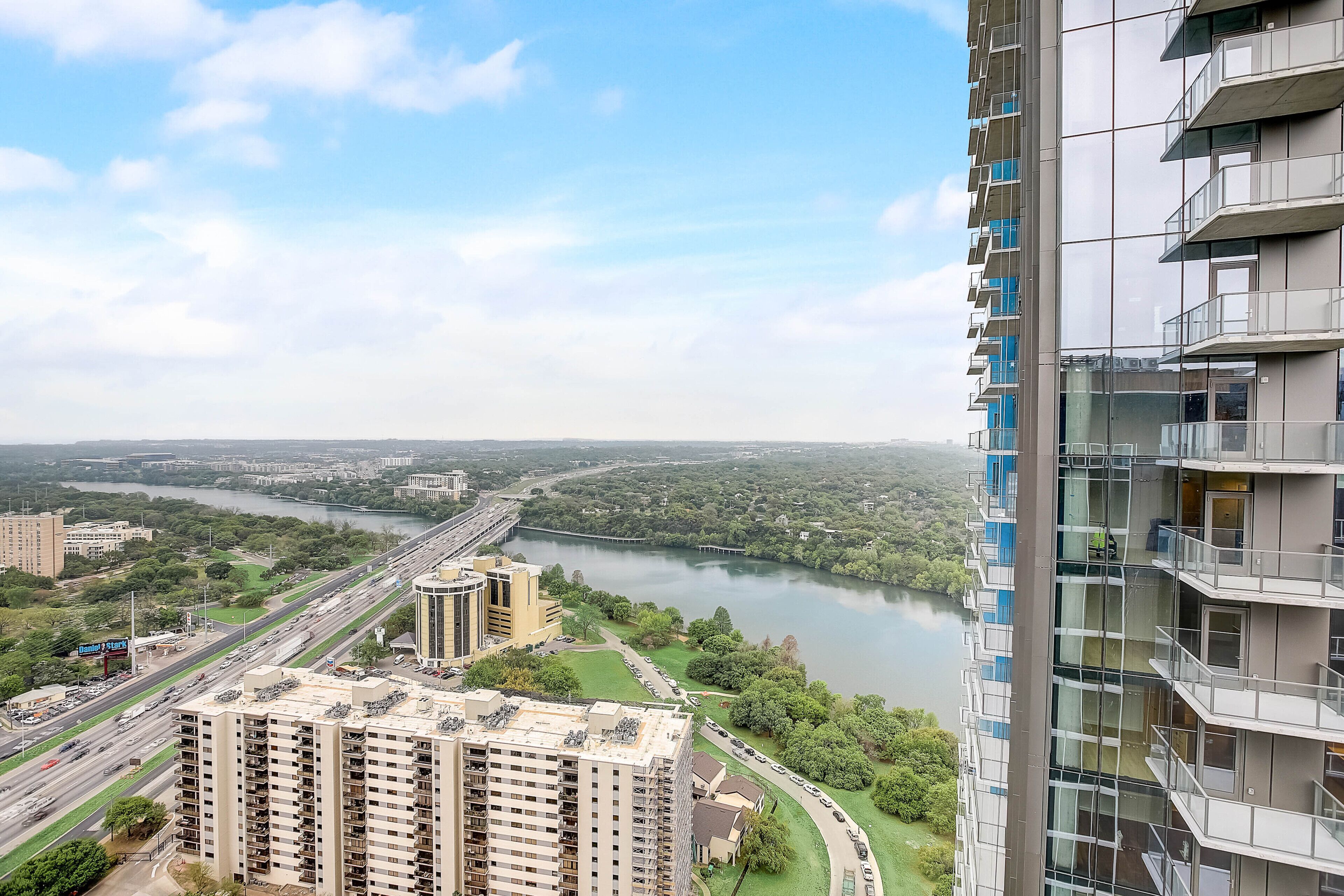 A high-rise building with multiple balconies overlooking a river and a highway.