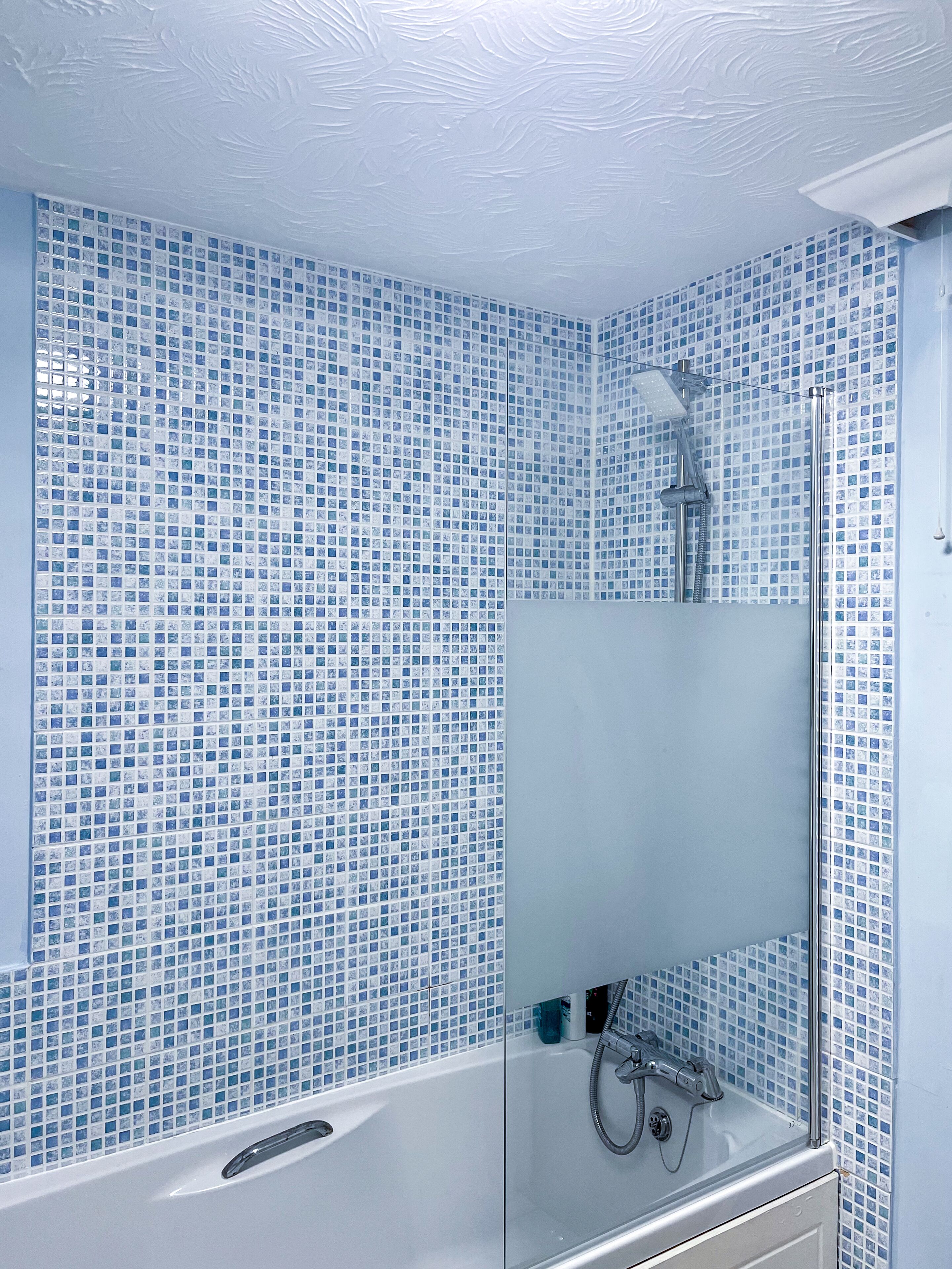 A bathroom with a glass-enclosed shower, tiled walls, and a white bathtub.