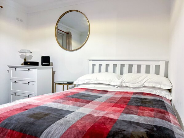A bedroom with a bed, white dresser, round mirror, and a small table.