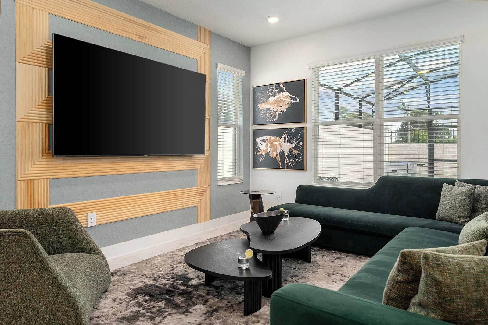 Una sala de estar moderna con un televisor de pantalla plana grande montado en una pared de paneles de madera, un sofá verde, una mesa de centro redonda y obras de arte en la pared.