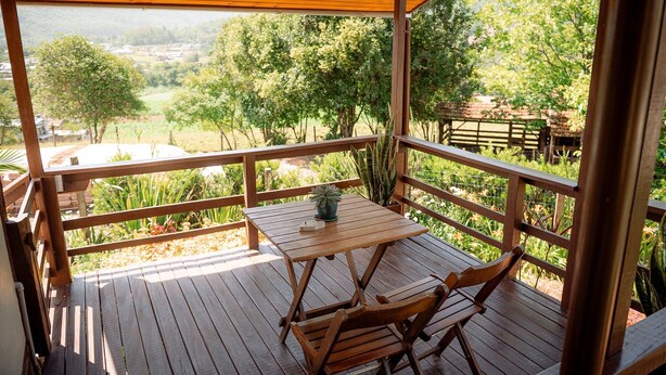 Una terraza de madera con mesa y sillas, con vista a un paisaje rural con árboles y un pueblo lejano.