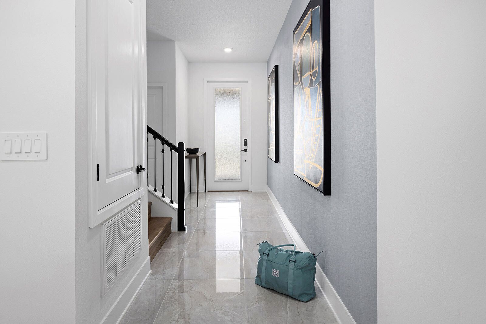 A hallway with a staircase, a door at the end, and a bag on the floor.