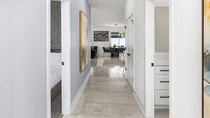 A modern hallway with a dining area in the background, featuring a clean, minimalist design with neutral colors and a tiled floor.
