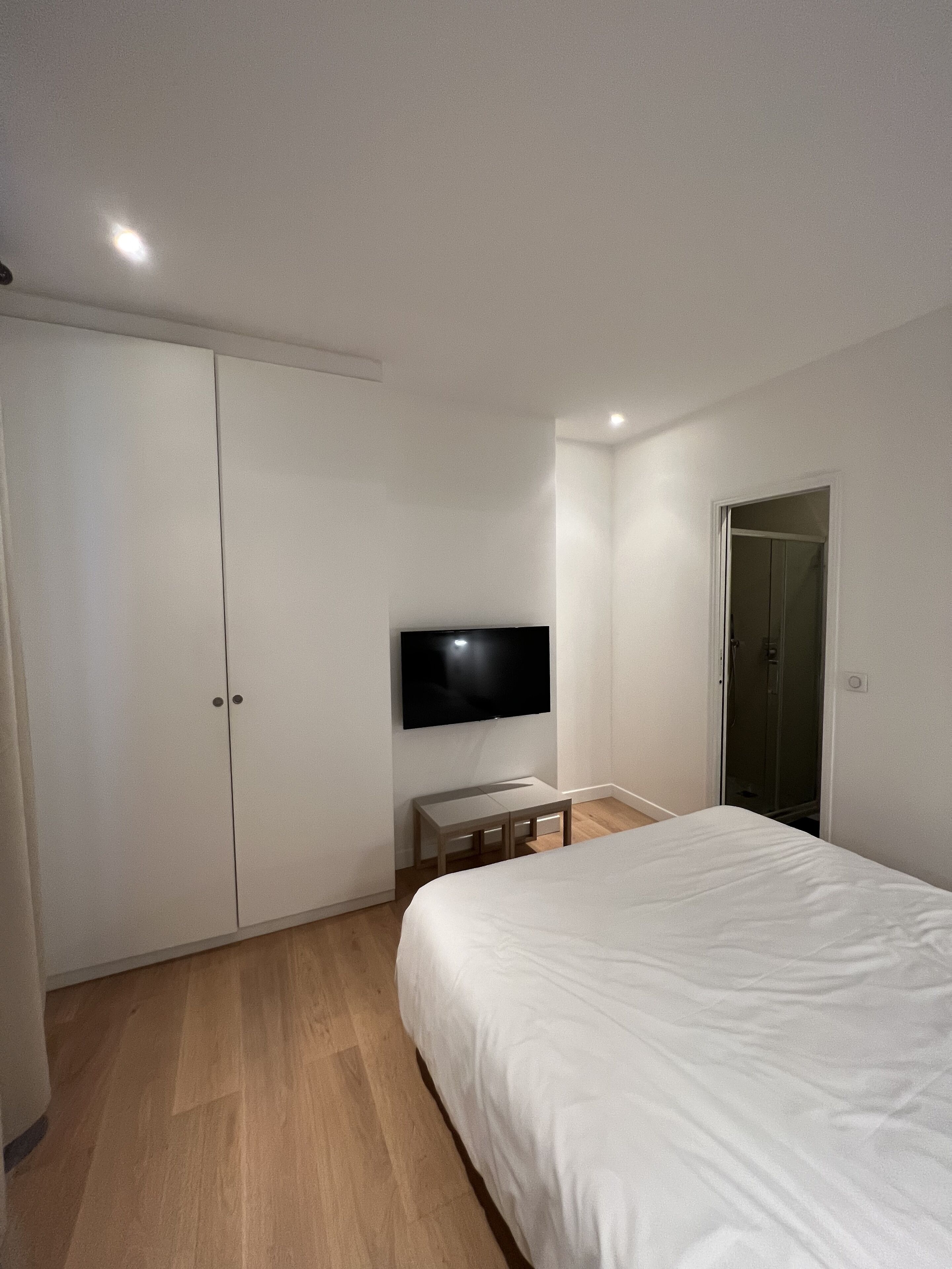 A bedroom with a bed, a TV mounted on the wall, a wardrobe, and a door.