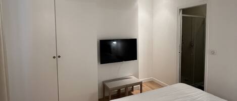 A bedroom with a bed, a TV mounted on the wall, a wardrobe, and a door.