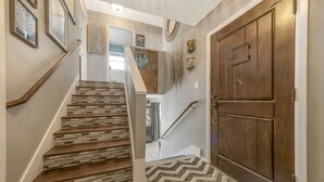 Un escalier avec des finitions en bois et des marches à motifs, menant à une pièce dotée d’une grande porte en bois et d’un tapis à motifs en chevrons.