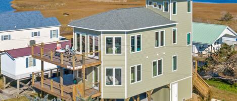 A multi-story house with a deck, a covered porch, and a view of a marshy landscape.