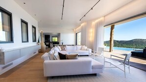 Ein modernes Wohnzimmer mit einem großen weißen Sofa, einem Couchtisch und Blick auf einen Pool und Berge.