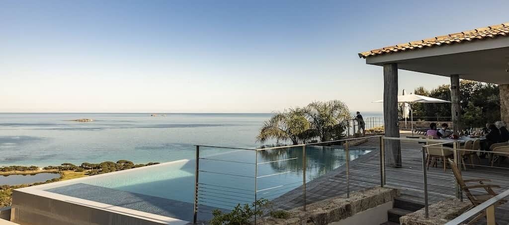 Zona junto a la piscina con vista al mar, un espacio cubierto para sentarse y una terraza de madera.