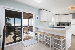 Una cocina moderna con armarios blancos, una barra con taburetes y vistas al océano a través de un ventanal corredero.