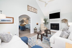 Una sala de estar moderna con chimenea, un televisor montado en la pared y un letrero que dice 'BEACHHOUSE'.