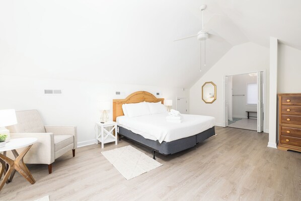 Un dormitorio con cama, una silla, una mesita de noche, un aparador y un ventilador de techo.