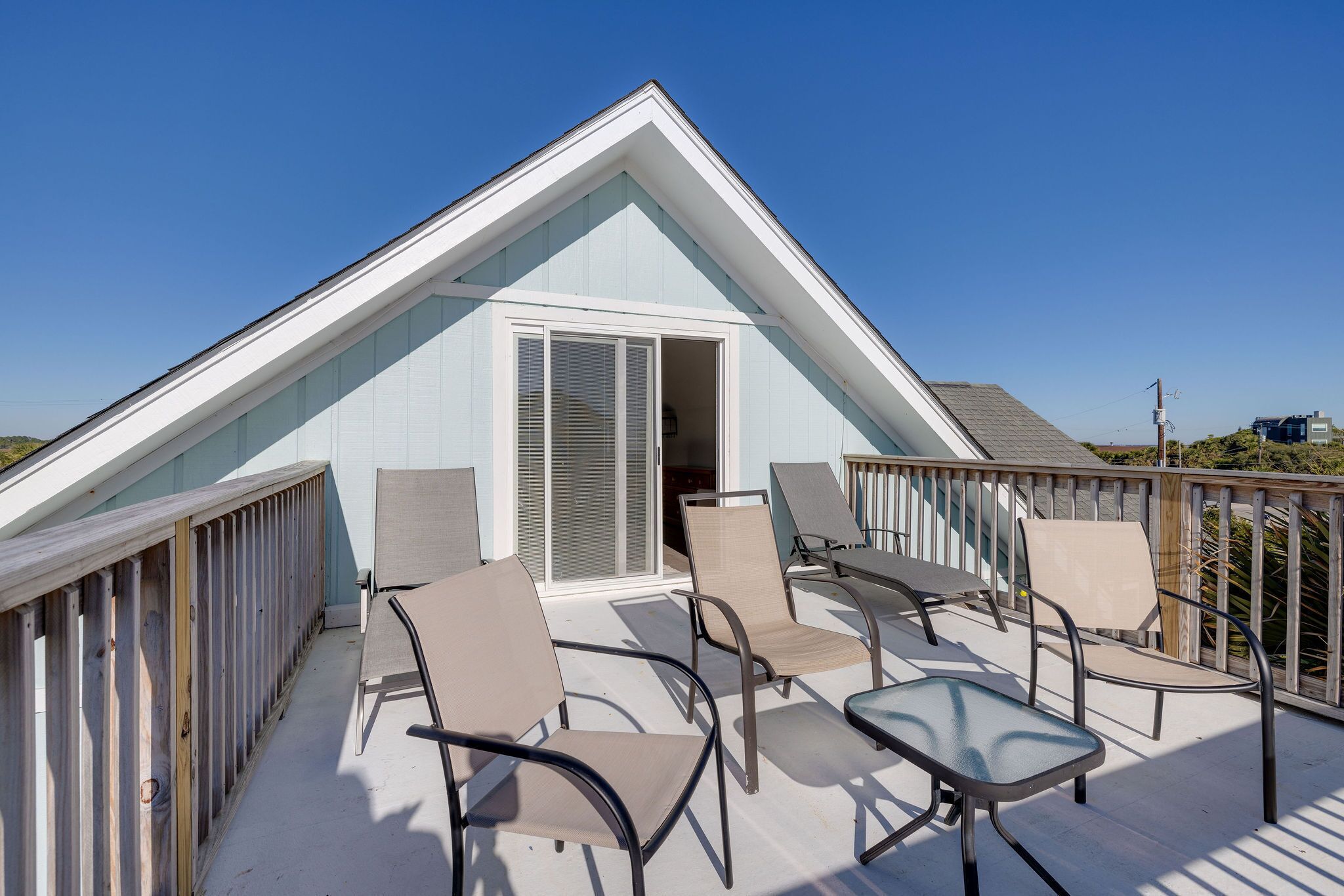 Una casa moderna con techo inclinado, una terraza con mobiliario exterior y un cielo azul despejado.