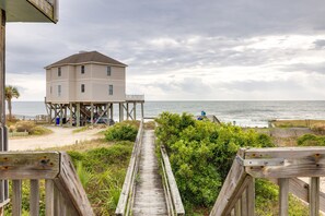A wooden pier leading to a white building with a balcony, overlooking the ocean. - Beach Bungalow - freshly remodeled, oceanfront oasis! (Folly Beach)