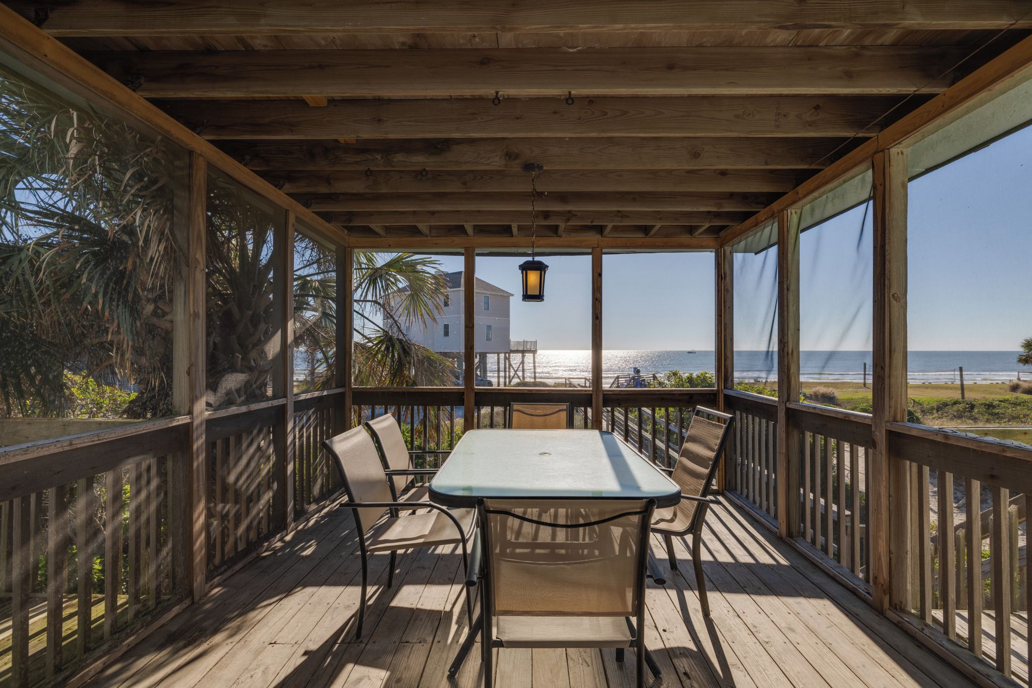 A wooden deck with a table and chairs, overlooking a beach and ocean.