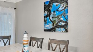 A dining area with a marble table, chairs, a decorative lighthouse model, and a painting of a lighthouse. - Steps to East Beach & Pet Friendly w/ 2 King Beds (St. Simons Island)