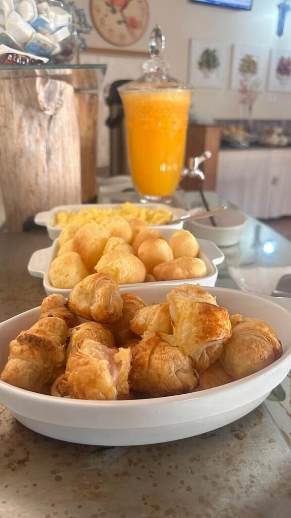 A breakfast setting with pastries, a glass of orange juice, and a bowl of scrambled eggs. - pousada ararinha azul (Campos do Jordão)