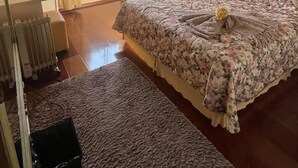 A bedroom with a wooden ceiling, a bed with floral bedding, a chair, a radiator, and a window with curtains. - pousada ararinha azul (Campos do Jordão)
