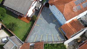 An aerial view of a parking lot with marked spaces, adjacent buildings with tiled roofs, and a grassy area. - pousada ararinha azul (Campos do Jordão)