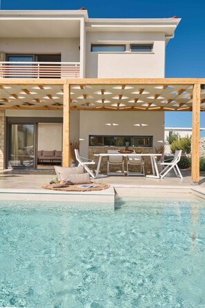 Een modern huis met een zwembad, zitplaatsen buiten en een pergola.