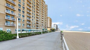 A beachfront hotel with a long, straight walkway leading to the beach, multiple balconies, and a clear view of the ocean.