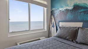 A bedroom with a large window, a bed with patterned bedding, and a wall mural of a wave.