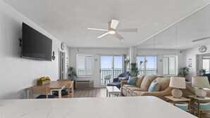A spacious living area with a large white table, a sofa, and a ceiling fan.