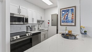 A modern kitchen with white cabinetry, stainless steel appliances, and a marble countertop.