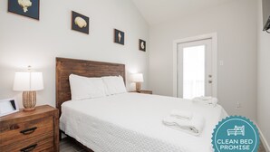 Une chambre propre et bien éclairée, avec une tête de lit en bois, du linge de lit blanc et une table de chevet avec une lampe.