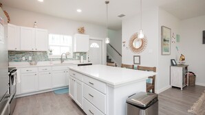 Une cuisine moderne avec des meubles blancs, un grand îlot central, des appareils en acier inoxydable et un plancher en bois.