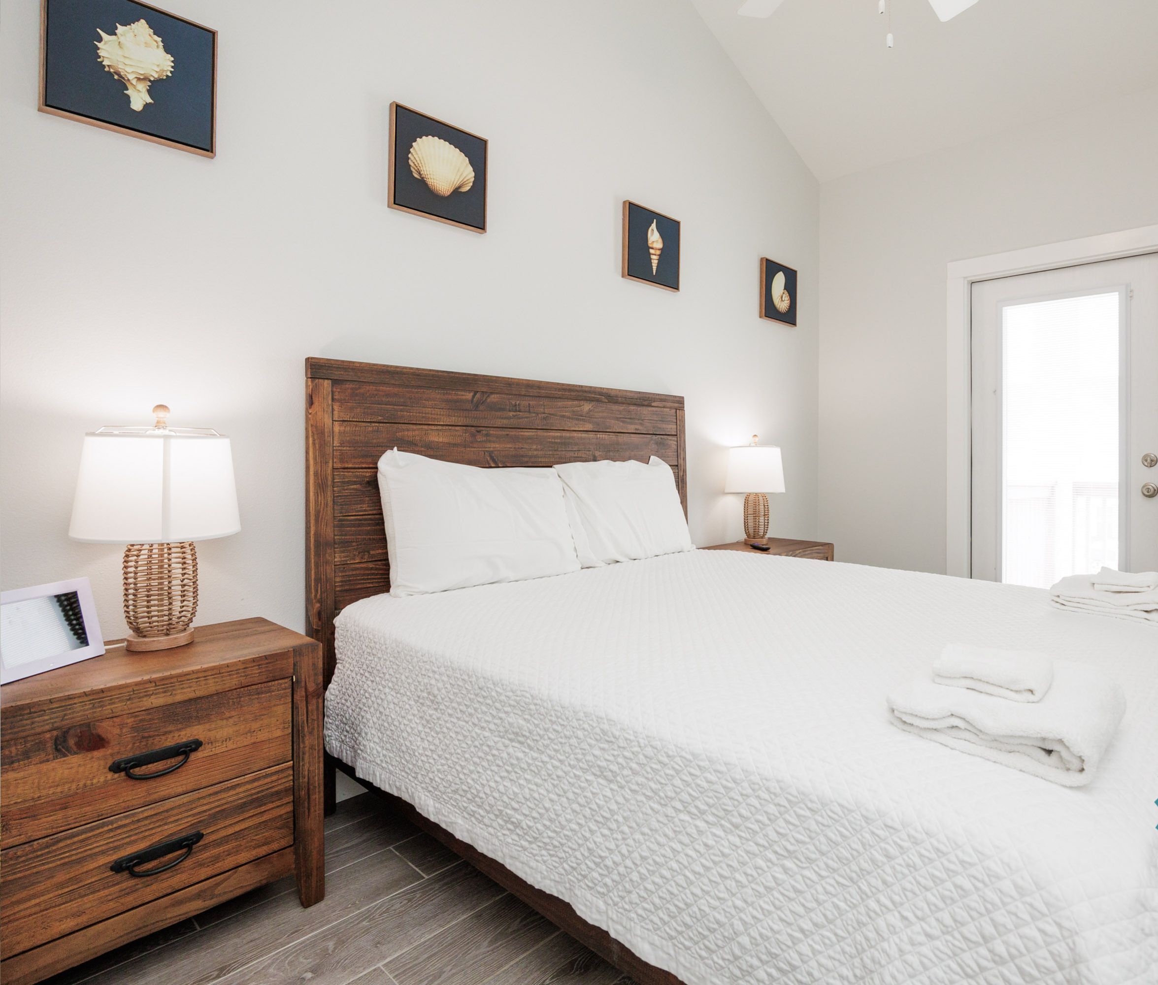 Un dormitorio limpio y bien iluminado con cabecera de madera, ropa de cama blanca y mesita de noche con lámpara.