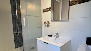 A modern bathroom with a glass-enclosed shower, a white vanity with a mirror, and a wooden stool. - La Maisonnette de Fred et Marie (Andernos-les-Bains)