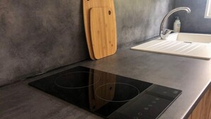 A modern kitchen with a built-in induction cooktop and a wooden cutting board. - La Maisonnette de Fred et Marie (Andernos-les-Bains)