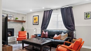 Ein modernes Wohnzimmer mit Kamin, Ledersofa und orangefarbenen Sesseln.