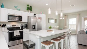A modern kitchen with white cabinetry, stainless steel appliances, and a central island with bar stools. - Family-Friendly Retreat | 2 Heated Pools, Slides & Pickleball (Corpus christi)