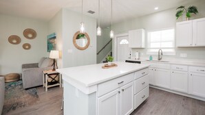 A modern kitchen with white cabinetry, a central island, pendant lights, and a staircase leading to another level. - Family-Friendly Retreat | 2 Heated Pools, Slides & Pickleball (Corpus christi)