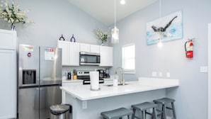 A modern kitchen with white cabinetry, stainless steel appliances, a large island with bar stools, and a hanging light fixture. - Spacious Coastal Retreat | Heated Pools, Slides & Resort Amenities (Corpus Christi)