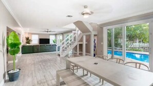 Un vaste espace intérieur comprenant une table à manger, un escalier et une piscine visible à travers de grandes fenêtres.