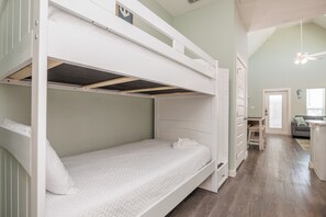 Une chambre avec un lit superposé, un bureau et une chaise, une petite salle de bain et un coin salon avec un canapé et une fenêtre.