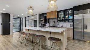 Een moderne keuken met een groot eiland, barstoelen, roestvrijstalen apparatuur en hanglampen.