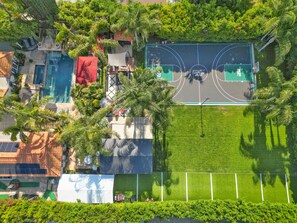 An aerial view of a property with a swimming pool, tennis court, and lush greenery.