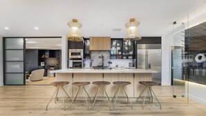 Een moderne keuken met een centraal kookeiland, barstoelen en hanglampen.