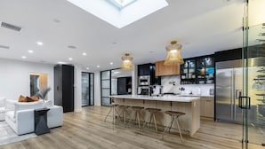 Een moderne keuken met een centraal kookeiland, barstoelen en een koelkast met glazen deur.