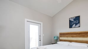 A bedroom with a large bed, a wooden headboard, a door with a view, and a wall-mounted sign. - Luxury Waterfront Retreat | 2 Heated Pools, Docks & Sunset Views (Corpus Christi)