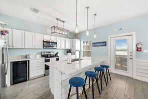 A modern kitchen with white cabinetry, stainless steel appliances, and a central island with bar stools.