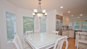Una cocina moderna con armarios blancos, una mesa de comedor con superficie de vidrio y un candelabro.