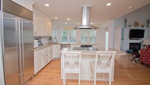 Una cocina moderna con muebles blancos, electrodomésticos de acero inoxidable y una isla central con dos taburetes de bar.