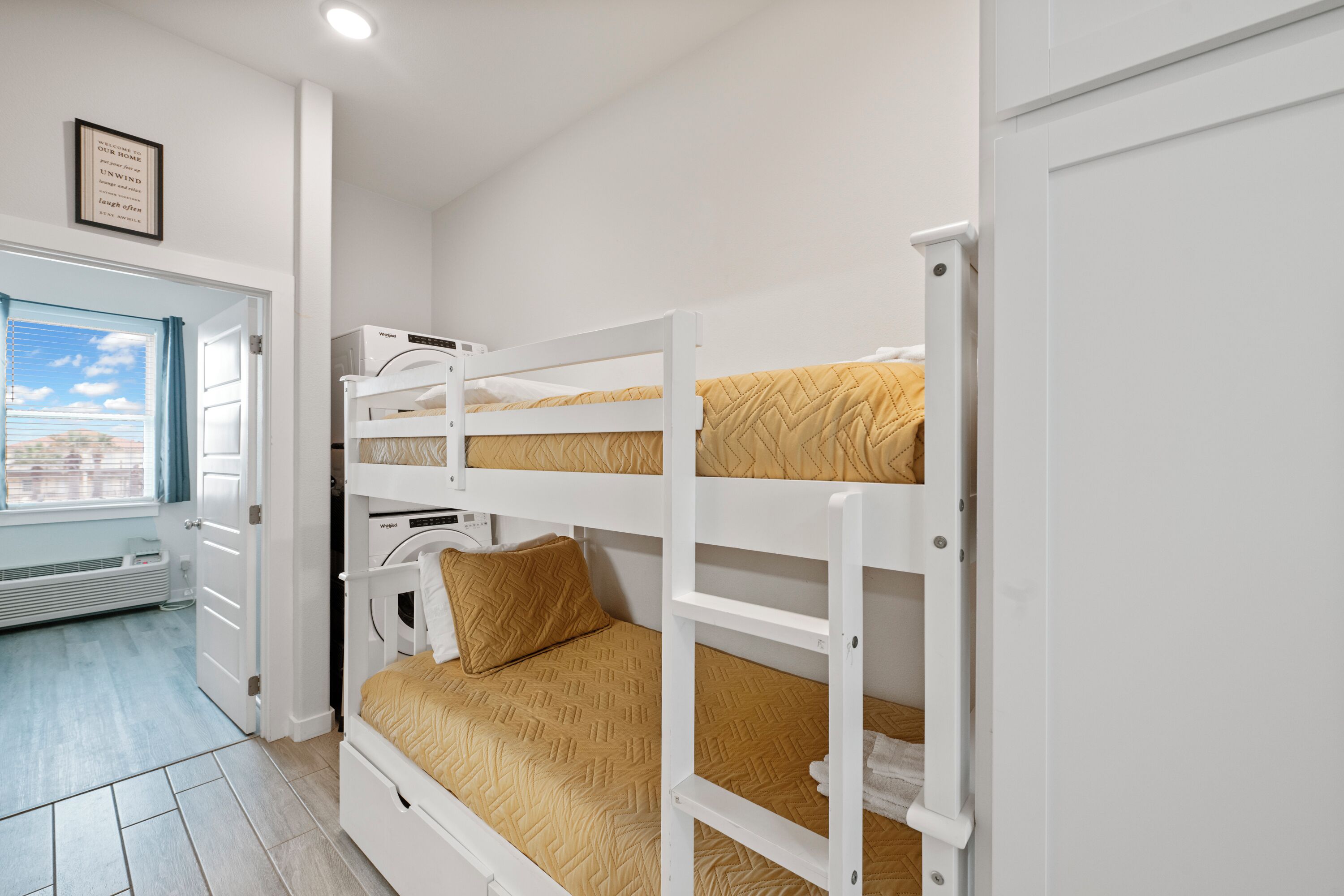 A bunk bed room with a window, a framed quote on the wall, and a door.
